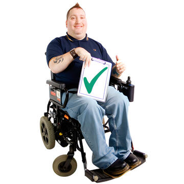 A man in a wheelchair with his thumb up and holding a piece of paper with a green tick on it.