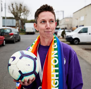 Sas Granville holding a football and wearing a Brighton and Hove Albion scarf