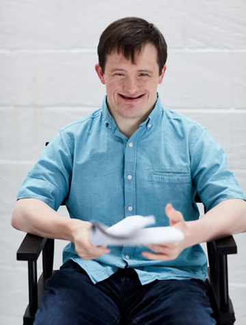 Tommy Jessop sitting in a directors chair with a script, smiling at the camera