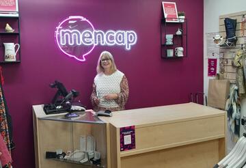 A woman standing behind a desk in a Mencap shop