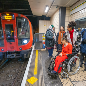 A photograph of a tube train coming into a station and a woman in a wheelchair on the platform