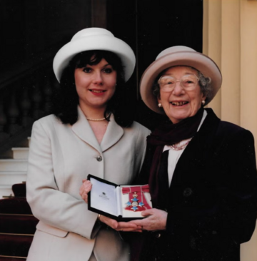 Judy holding up her MBE alongside another woman