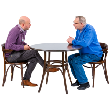 Two men sitting at a table.  One man is talking and the other man is listening.
