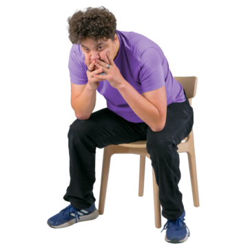 A man sitting on a chair with his elbows resting on his knees and his chin in his hands looking worried.