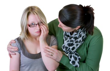 A woman with her arm around the shoulders of another woman who looks sad and is wiping her eye.