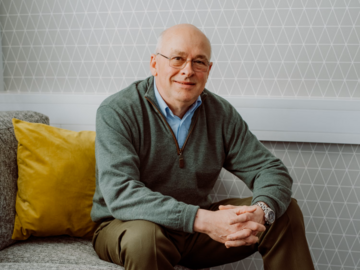 A man Phil Hughes, one of Mencap's trustees, sitting and smiling.