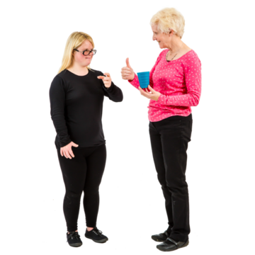A woman holding a cup in one hand and holding her thumb up with the other hand.  She is looking at a girl who is signing drink.