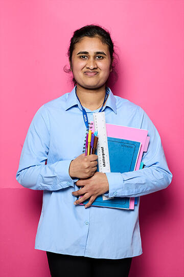 Diviyha holding some school books, pens and a ruler