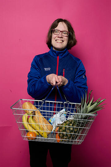 Janis in her Tesco uniform holding a shopping basket of fruit