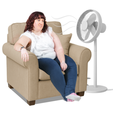 A woman sitting in an arm chair with a standing fan in front of her to keep cool