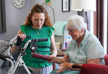 A support worker kneeling down helping a woman in a chair with her purse