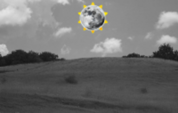 A hill and trees in black and white with the Moon in the sky.  There is a little bit of Sun behind the Moon.