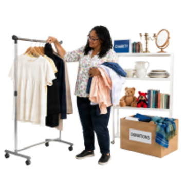A woman hanging up clothes on a rail.  Behind her are shelves with items on them and a box which says donations.