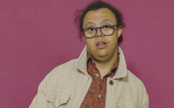 Michael Beynon wearing a cream jacket in front of a dark Mencap pip background