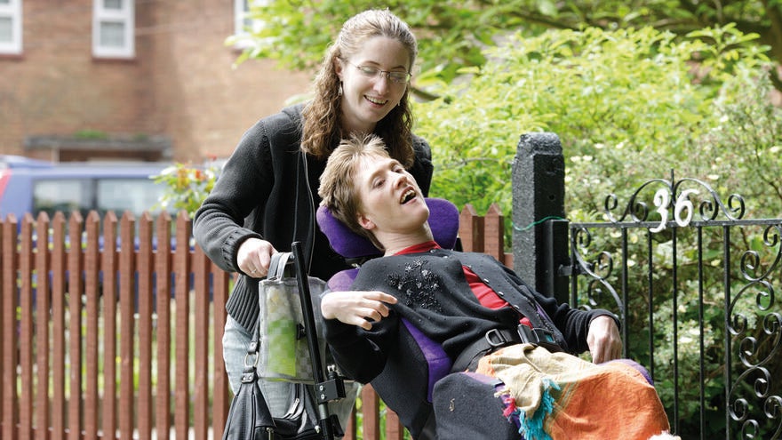 Two women outside together. One woman is pushing the other who is using a wheelchair.