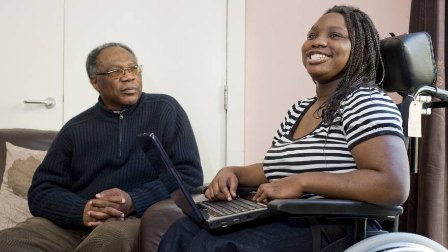 Young woman sat with her laptop, older man sat on sofa next to her