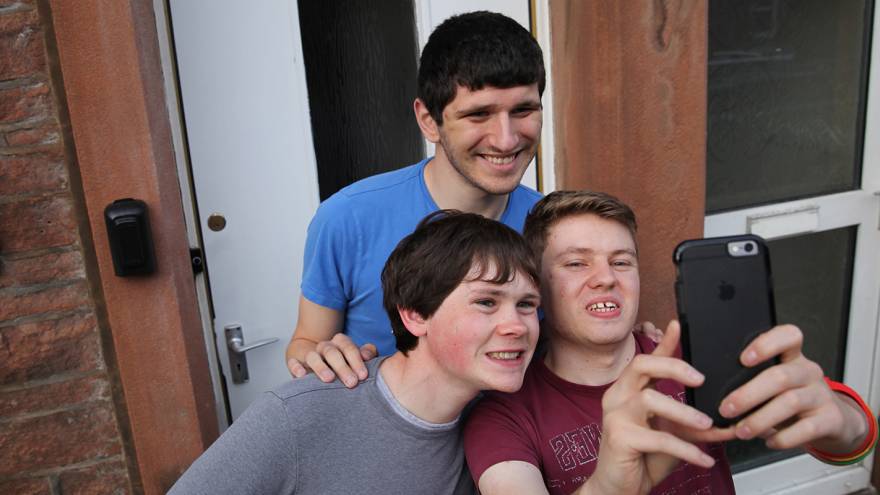 Three young men stood together posing for a selfi