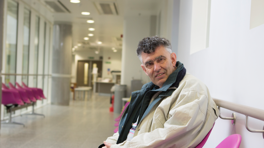 Older man wearing an overcoat sat in hospital waiting room