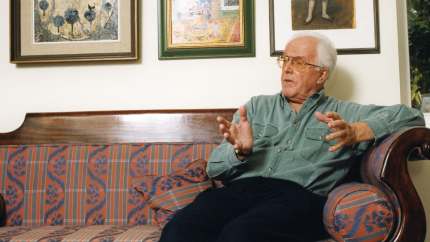 Man, Brian Rix, sat on sofa.