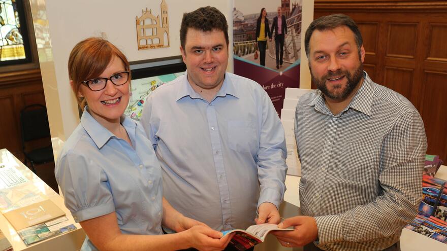 Three people stood together holding leaflet.