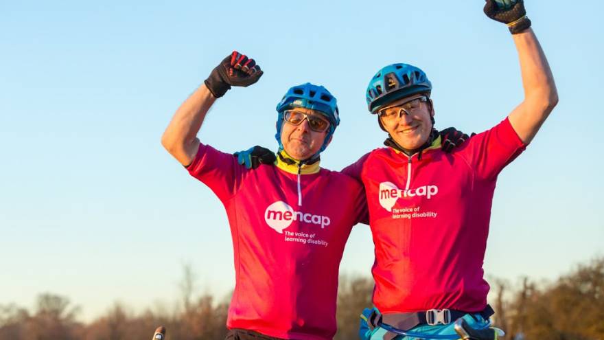 Two men on bikes holding their arms up in celebration