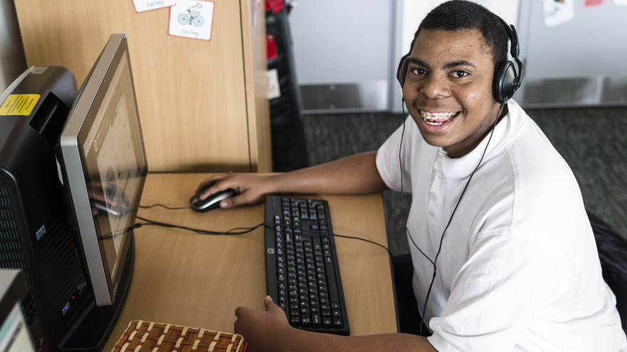 Young man sat smiling at computer wearing headphones