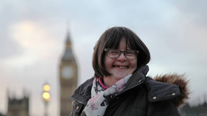 Woman with dark hair and glasses stood smiling at camera. Big Ben is in the background.