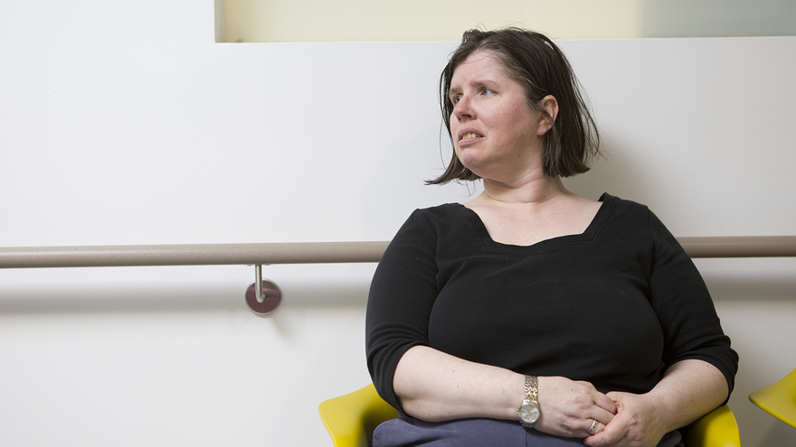 Woman with dark hair wearing black top sat in hospital waiting room.