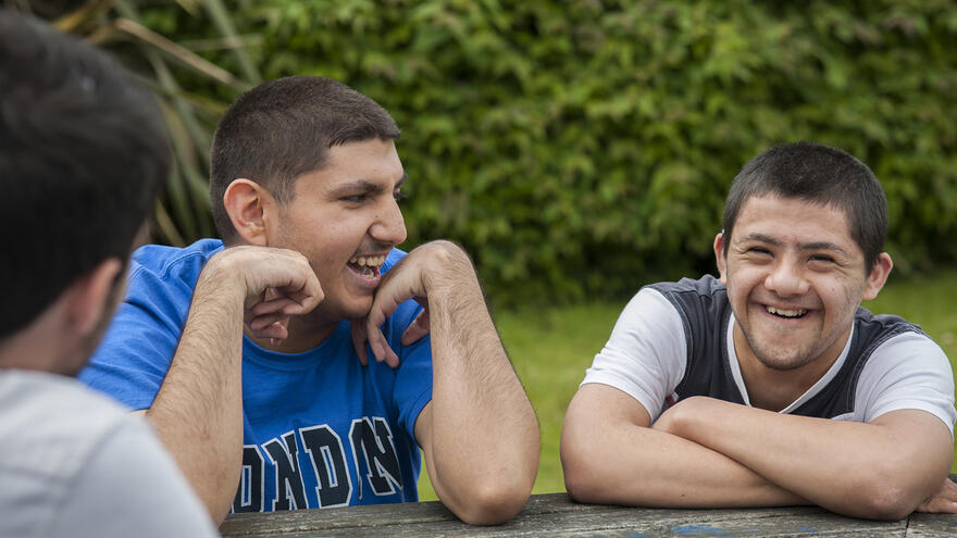Young men sat at table outside laughing