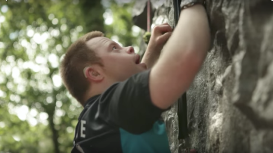 Young man outside climbing a wall on an assault course.