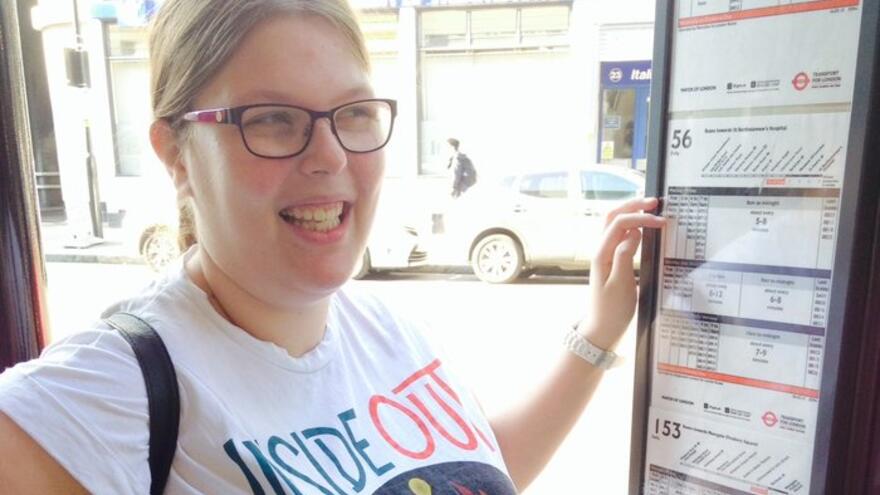 Woman with glasses stood at bus stop looking at timetable.