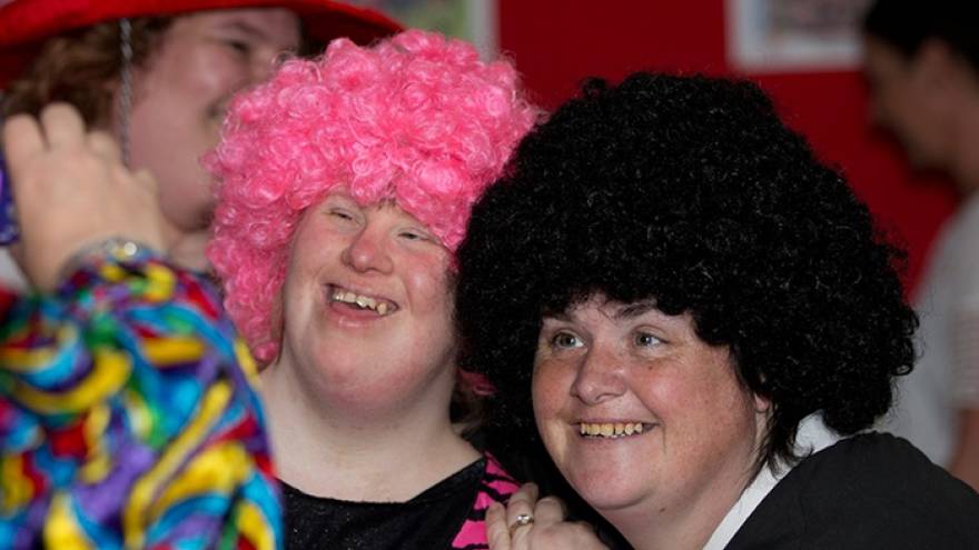 Two people wearing large colourful wigs stood next to each other at party.
