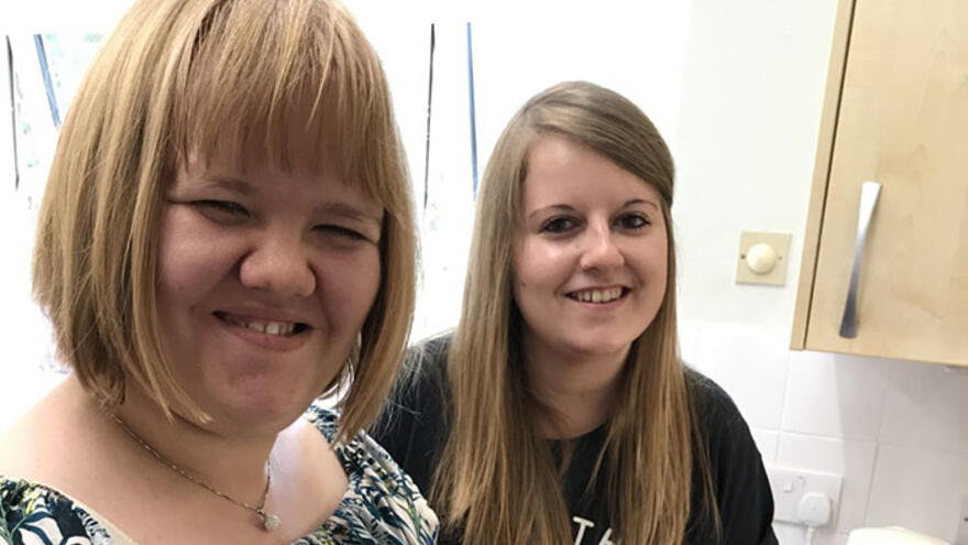 Two women stood in kitchen smiling.