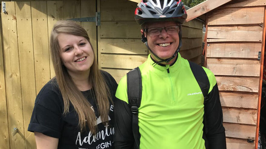 Man and woman stood outside. The man is wearing a high visibility top and a bike helmet.