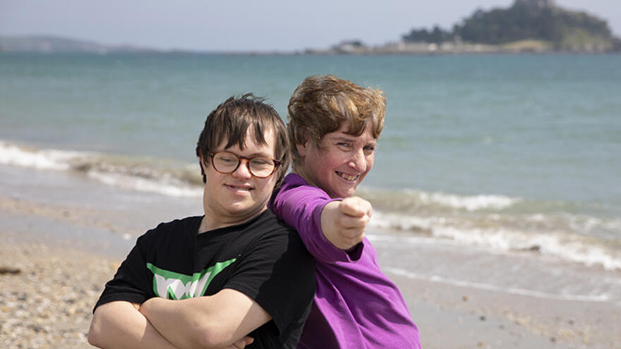 Two people stood back to back on a beach