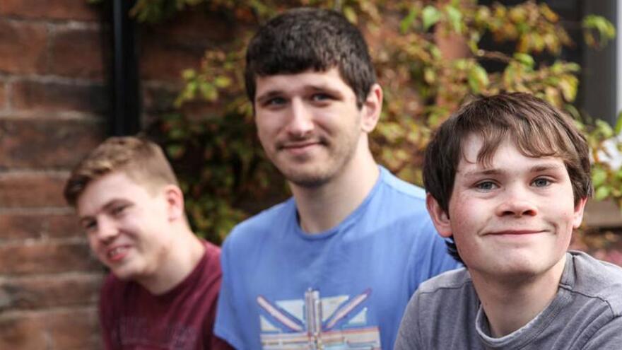 Three young man together in front of brick wall
