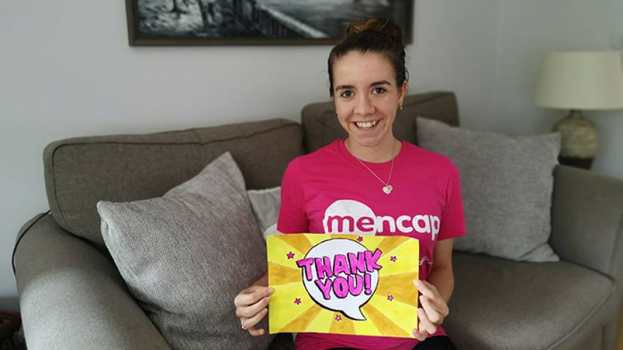 Young woman sat on sofa holding a "thank you" sign