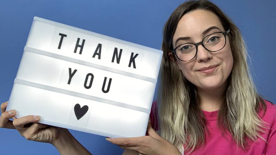 Young woman wearing glasses holding a lightbox with letters on that reads "thank you"