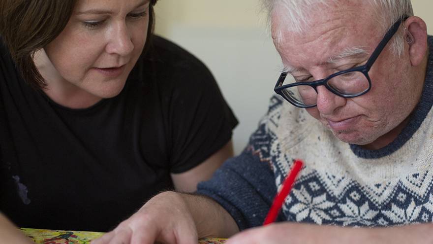 Woman sat at table with older man doing craft activities together