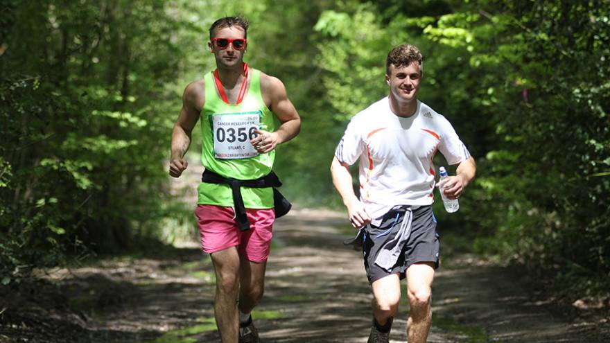 Two men running together through woodland countryside path.