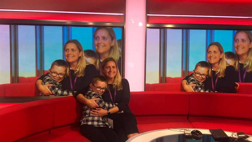 Woman, Caroline White, with her son, Seb, sat together on BBC Breakfast sofa in tv studio.