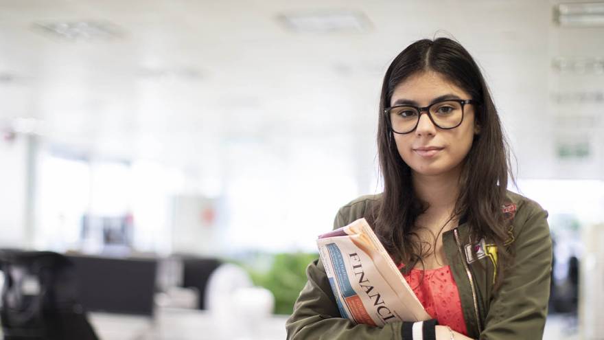 Young woman stood in an office holding a copy of the Financial Times newspaper.