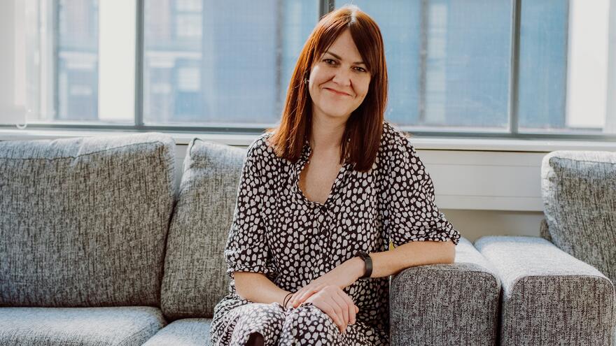 Photograph of a woman, Kathryn Rees, sitting on a sofa smiling