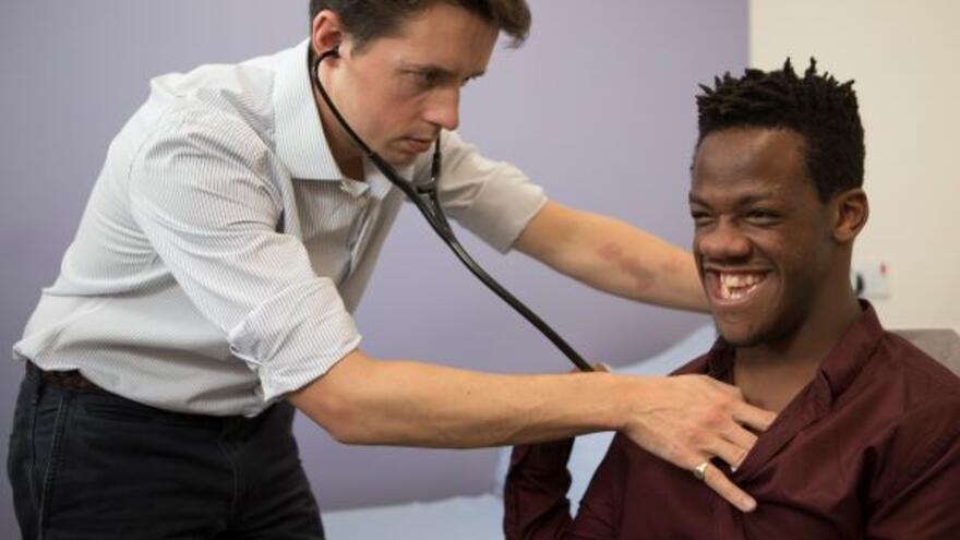 Photograph of a man, Brendan, sitting down having his heart rate monitored by a doctor who is standing and using a stethoscope 