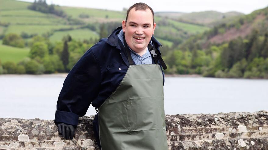 Robert standing in front of a stone wall with a lake beyond