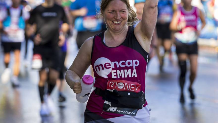 Woman running with one hand punching the air, wearing a Mencap fundraising race vest