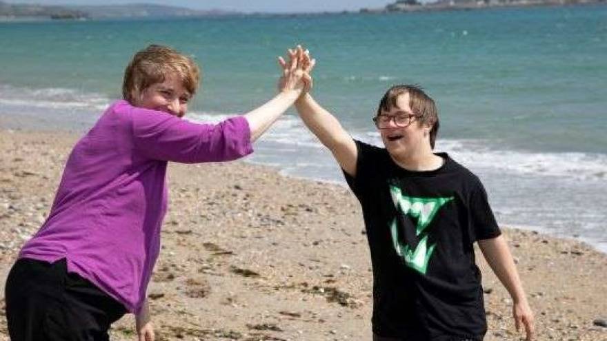 Woman doing a high-five with a young man with downs syndrome. They are smiling and standing on a beach