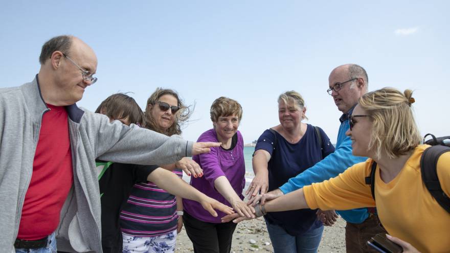 A group of people on a beach with their hands outstretched and joined in a circle