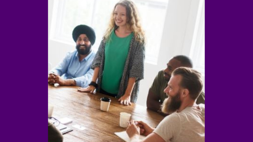 Three people sitting at a table and one person standing up talking