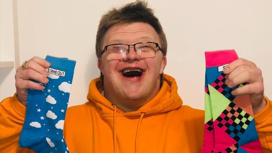Ross who has down's syndrome holding up a colourful, odd pair of socks by 'Stand Out Socks'